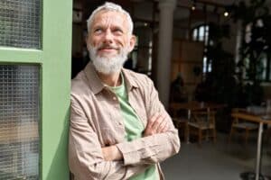 Elderly man leaning against a wall smiling.